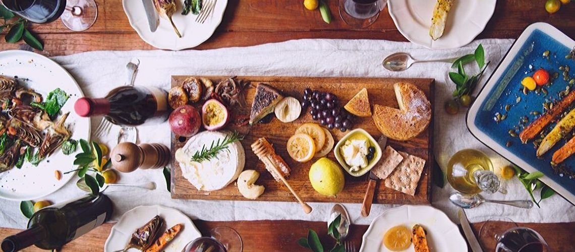 Mesa com vários tipos de comida, saudáveis ou não, pratos e taças de vinho